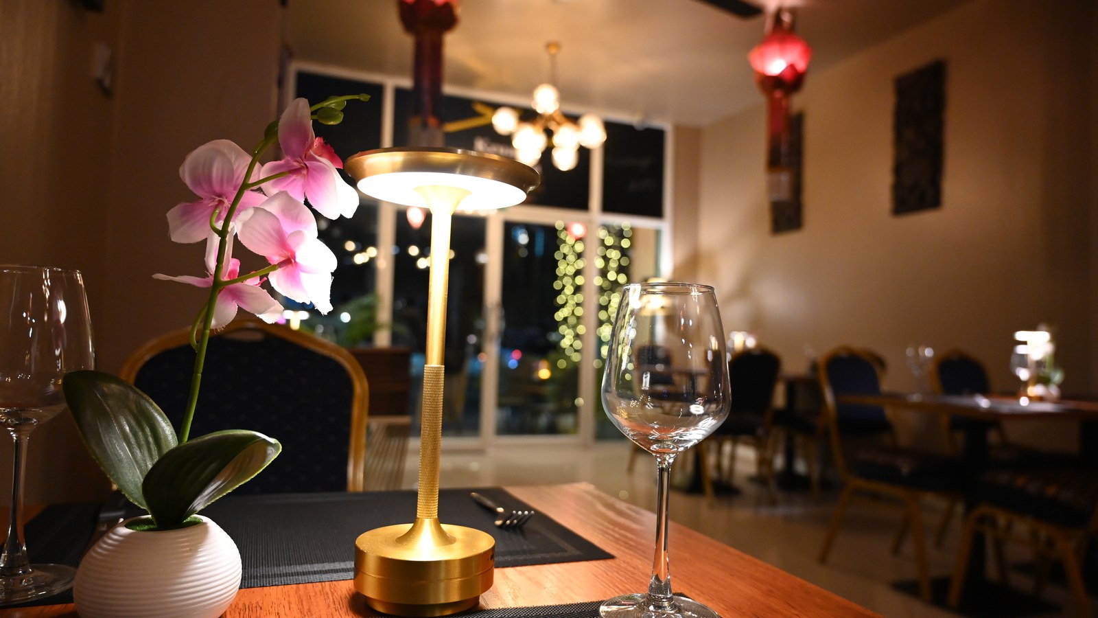 夜のレストランのテーブル。ランプと蘭の花、空のワイングラス